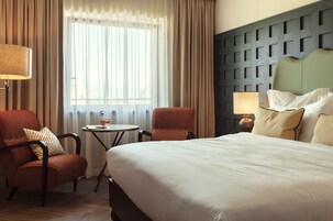 Ein Hotelzimmer mit einem großen Bett, zwei Sesseln, einem kleinen runden Tisch und einer Lampe.