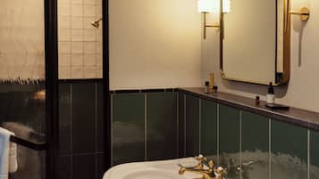 A bathroom with a white sink, gold fixtures, a large mirror, and green tiled walls.