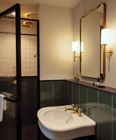 A bathroom with a white sink, gold fixtures, a large mirror, and green tiled walls.