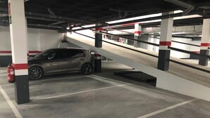 A parking garage with a car parked in a spot, concrete pillars, and a fire extinguisher.