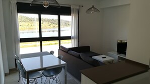 A modern living space with a dining area, a sofa, a TV, and a view of a lake.