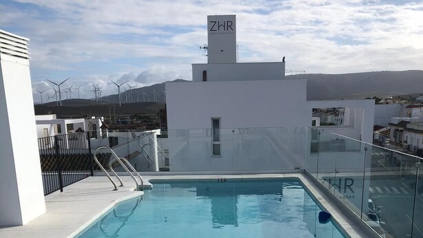 A swimming pool with a clear blue water, a white building with a sign 'ZWR', and a metal railing.