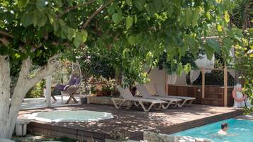 A pool area with lounge chairs, a hot tub, and a pergola with a swing chair.
