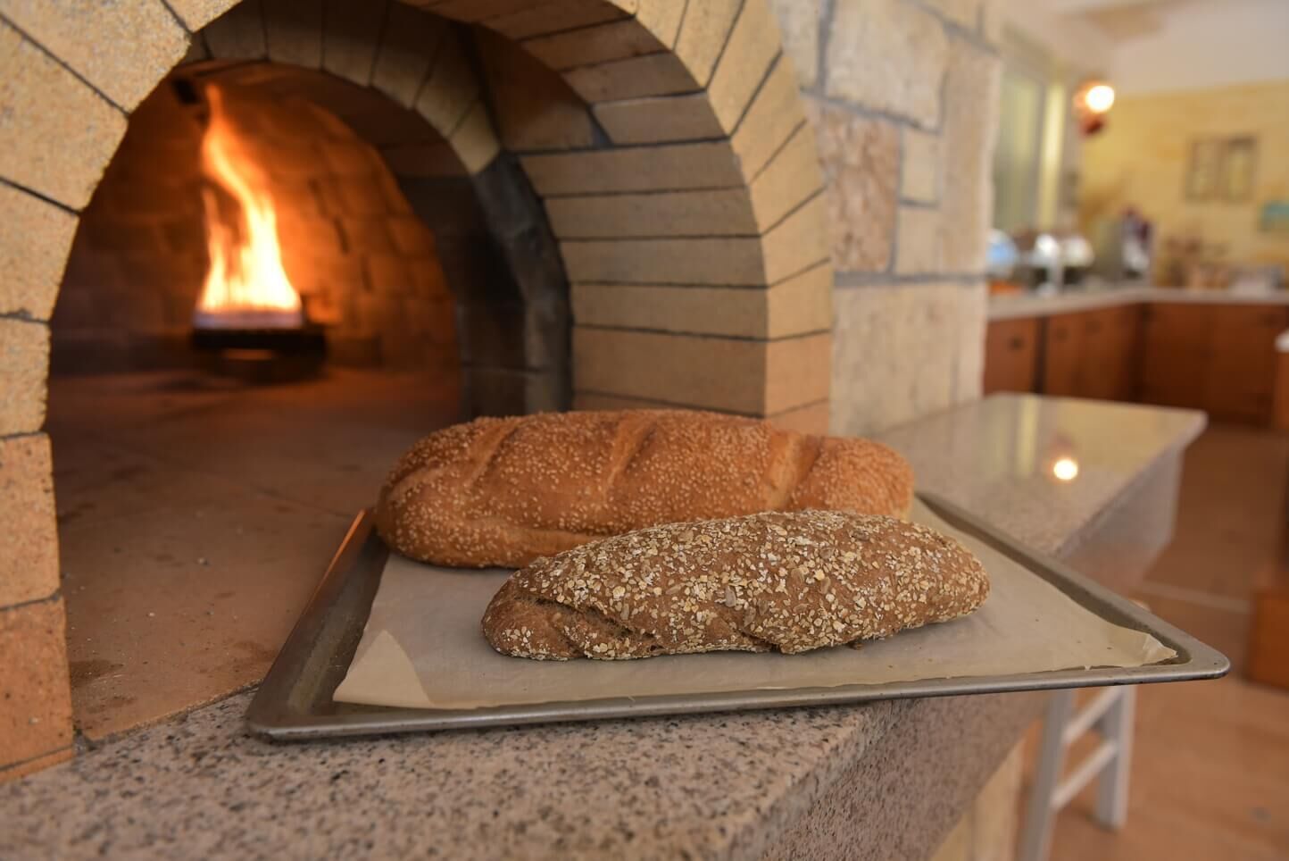 Two loaves of bread on a metal tray in front of a brick oven with a fire.