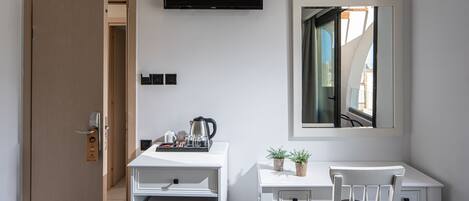 A compact hotel room with a kitchenette, a desk, a chair, a TV, and a mirror.