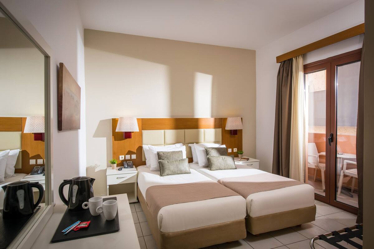 A hotel room with two beds, a desk with a coffee maker, mugs, and a tray with pens and a phone.