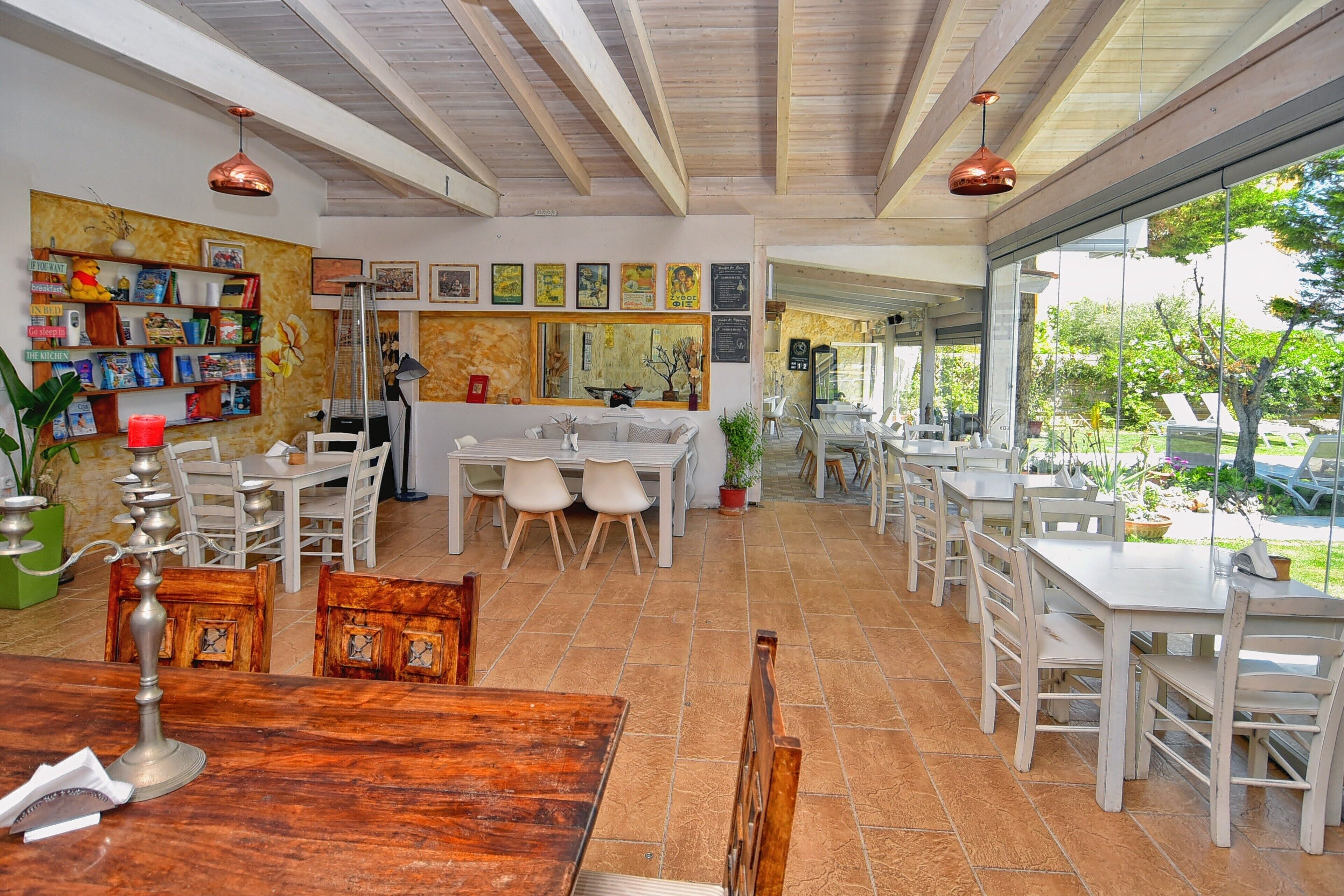 Uma sala de jantar ampla com várias mesas e cadeiras, uma ilha central com pia, e vista para o jardim exterior.