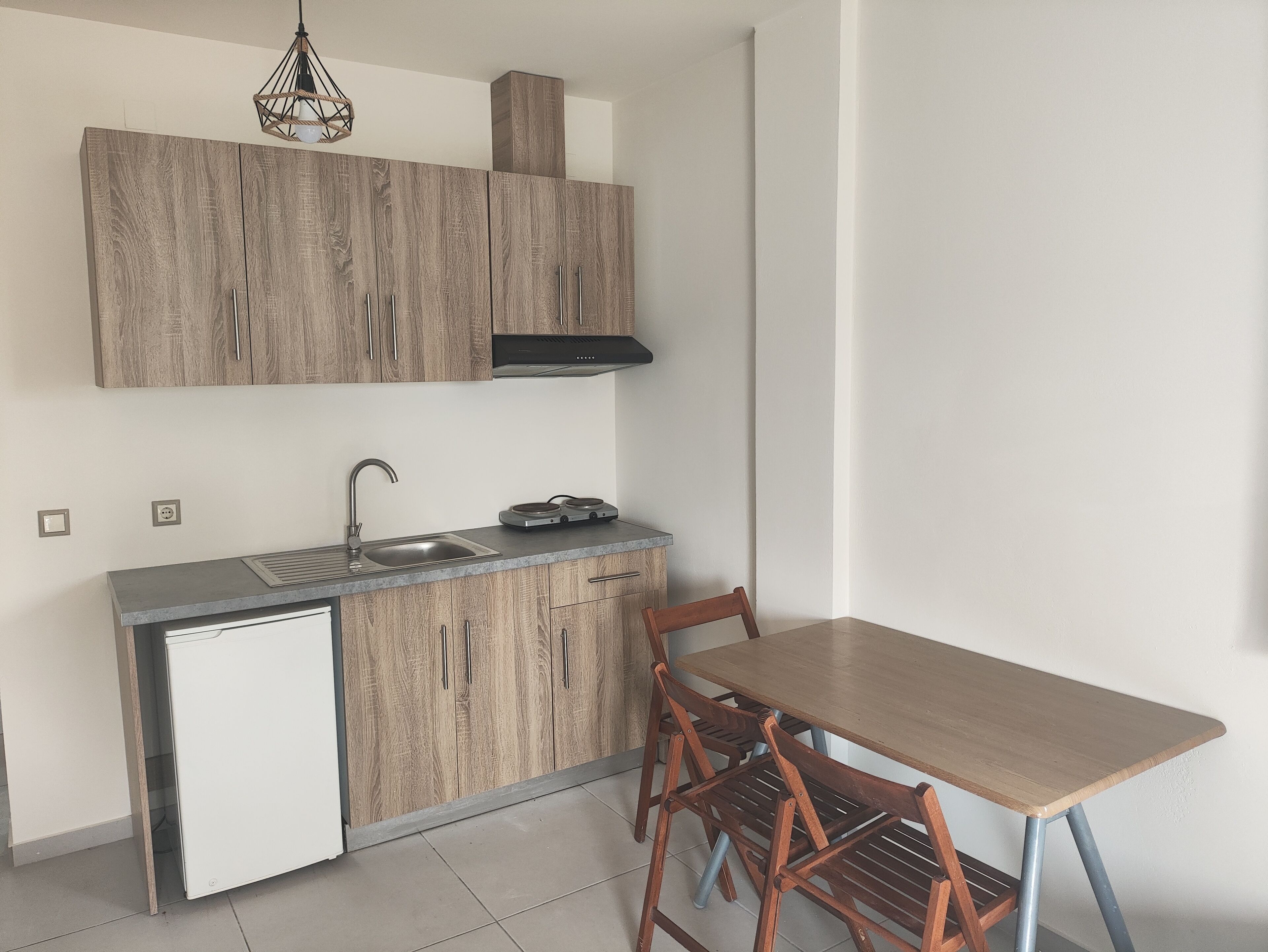 Cocina compacta con armarios de madera, lavavajillas integrado, un lavabo y comedor con mesa y sillas.