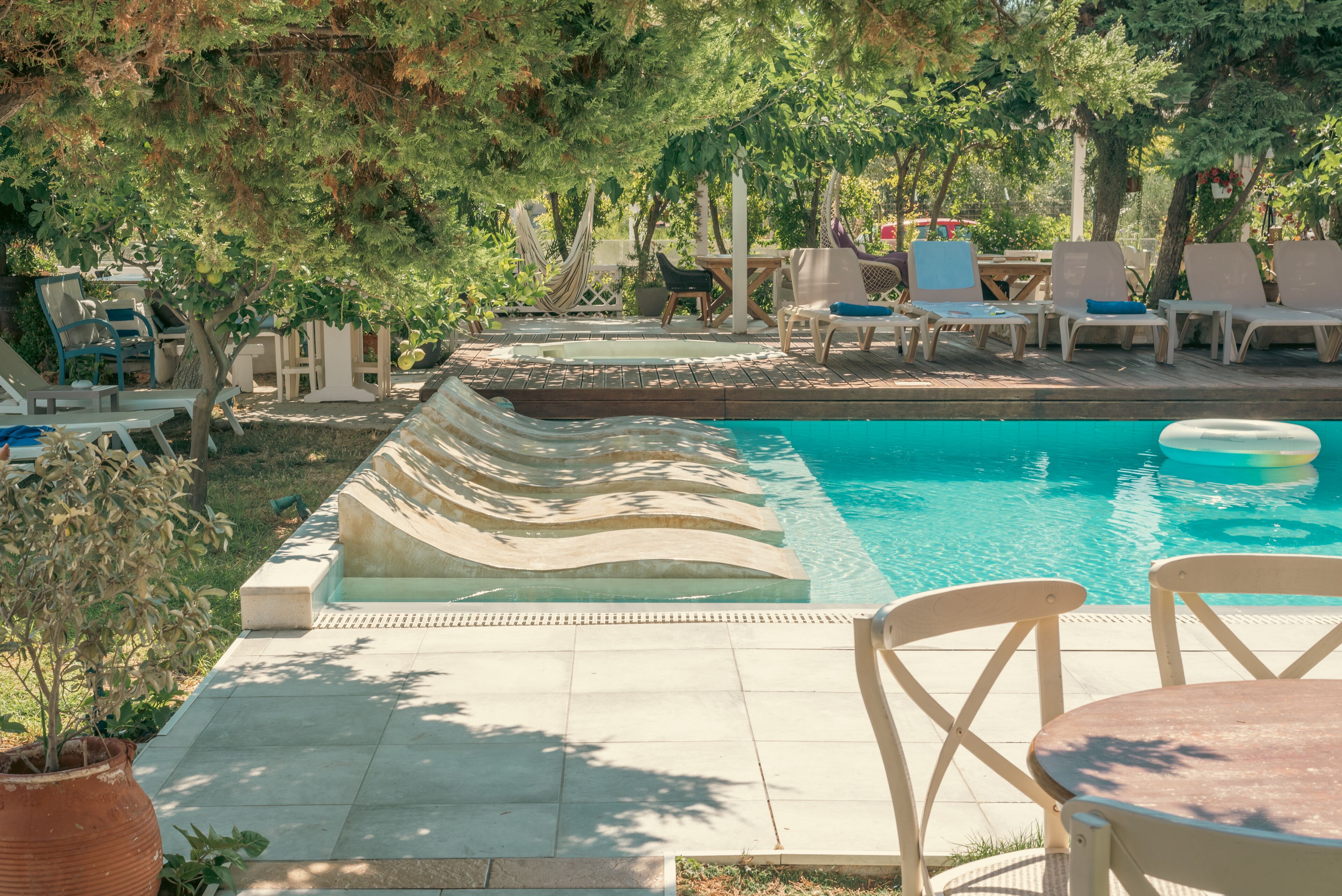 Una piscina con sillas de descanso y una mesa, rodeada de árboles y vegetación.
