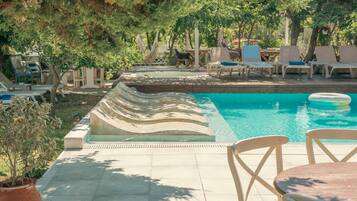 Una piscina con sillas de descanso y una mesa, rodeada de árboles y vegetación.