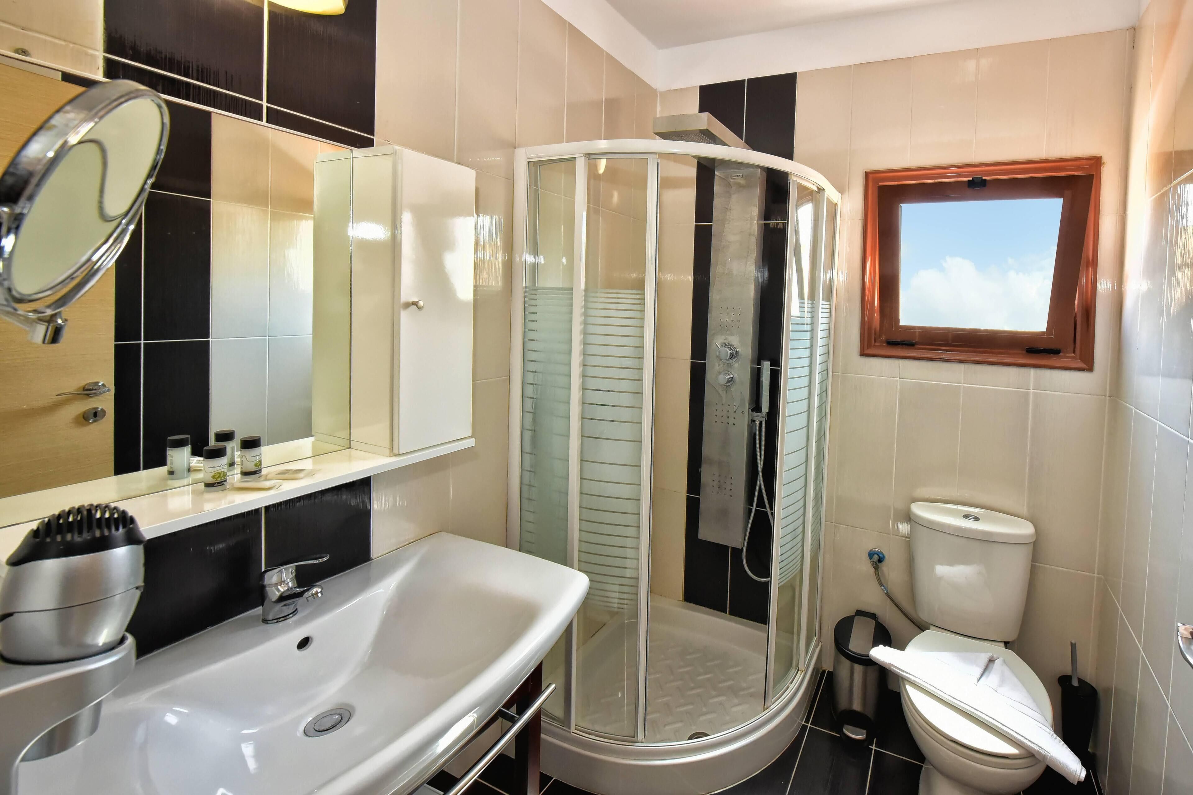 Un baño con ducha de vidrio, lavamanos, inodoro y ventana.