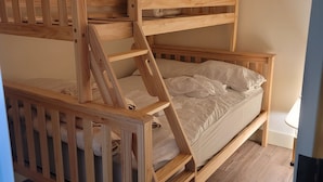 A wooden bunk bed with a ladder, a white mattress, and a wooden floor.