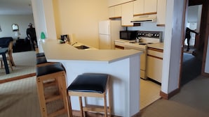 A compact kitchen with a central island, wooden stools, and basic appliances.