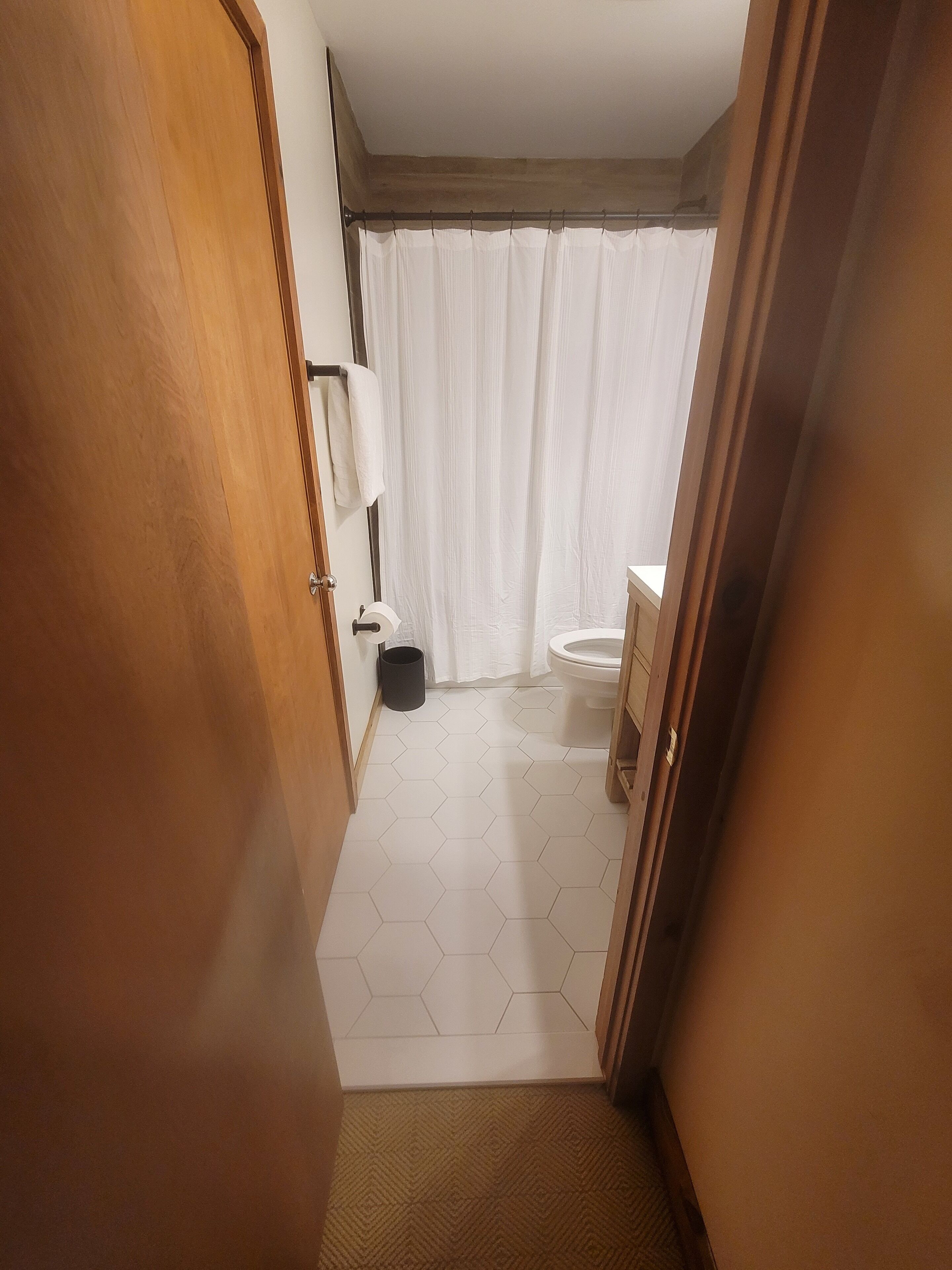 Ein schmaler Flur, der zu einem Badezimmer mit Toilette, Duschvorhang und Mülleimer führt.