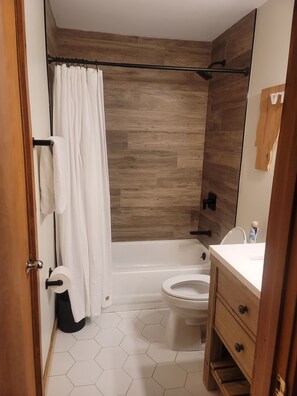 A modern bathroom with a wooden wall, a bathtub, a toilet, and a vanity with drawers. - Ski on ski off condo (Stratton)