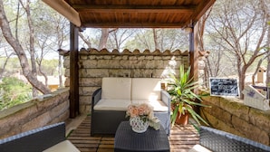 A covered outdoor seating area with a stone wall, a cushioned sofa, a wicker table, and a potted plant. - Charming "Villa Viola" close to the Beach with Sea View, Terrace & Garden (Narbolia)