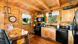 Ein Holzhütten-Interieur mit einer Küche, die Holzschränke, einen schwarzen Kühlschrank, eine Mikrowelle und einen Herd zeigt.