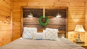 Ein Schlafzimmer einer Holzhütte mit einem Bett, zwei Wandleuchten, einem grünen Kranz und einer Nachttischlampe.