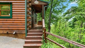 Eine Holzhütte mit einer Treppe, die zu einer Veranda führt, umgeben von üppiger Vegetation.