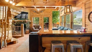 Ein Holzblockhaus-Interieur mit Kamin aus Stein, einer Bar und einer Sitzecke mit Sofa und Sesseln.