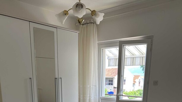 A bedroom with a large bed, a wardrobe, a mirror, and a window with curtains. - Apartment Ksenija (Supetar)