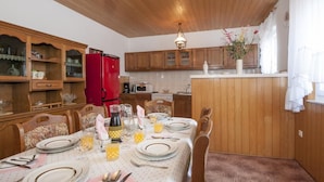 A dining area with wooden cabinets, a red refrigerator, and a table set for four with plates, glasses, and a vase of flowers. - Apartment Ksenija (Supetar)