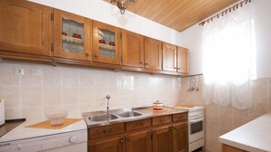 A kitchen with wooden cabinets, a white countertop, a sink, and a stove. - Apartment Ksenija (Supetar)