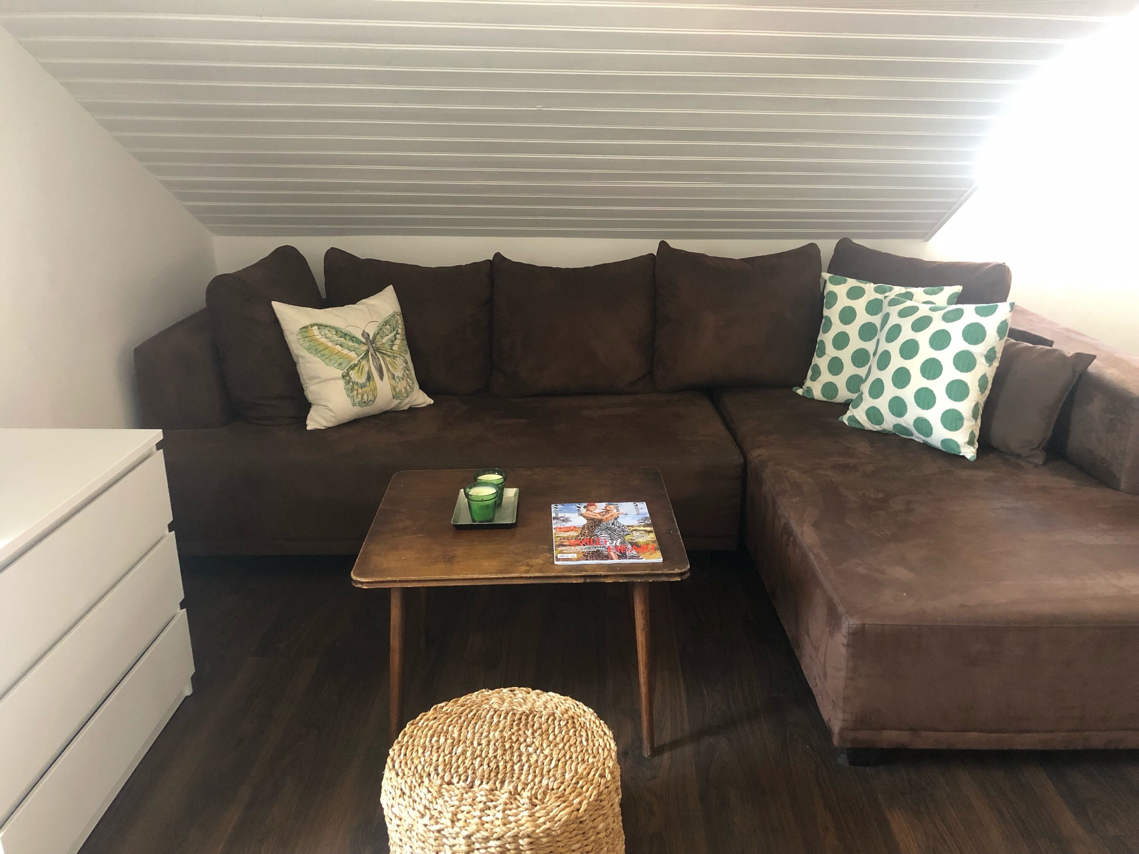 A cozy living room with a brown sectional sofa, a small wooden coffee table, and a woven ottoman.