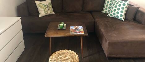 A cozy living room with a brown sectional sofa, a small wooden coffee table, and a woven ottoman.