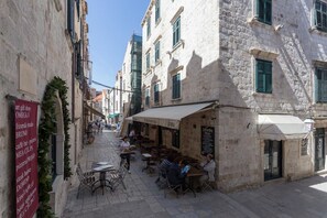 A narrow street with outdoor seating at cafes, stone buildings, and a sign listing local businesses. - Apartment Dubravka Iza Roka (Dubrovnik)
