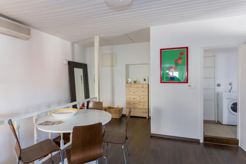 A modern, well-lit room with a round dining table, chairs, a wooden dresser, and a washing machine in the background.
