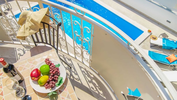 Un balcón con piscina, una mesa con frutero y copas de vino, y sillas de descanso.