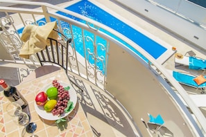 Uma varanda com piscina, mesa com uma fruteira e copos de vinho, e espreguiçadeiras.