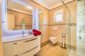 Une salle de bain avec un grand miroir, un lavabo, des toilettes et un espace douche.