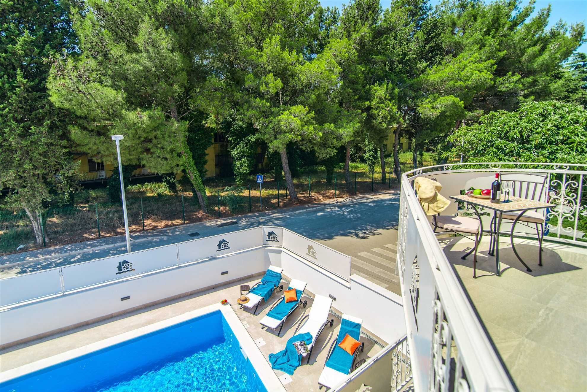 Un espace piscine aménagé sur le toit, avec des chaises longues et une table, entouré d’arbres et offrant une vue sur la rue.