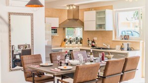 Una cocina moderna con comedor, que incluye una isla central, iluminación colgante y un espejo grande.