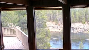 A room with three large windows overlooking a natural landscape with a river and forest.