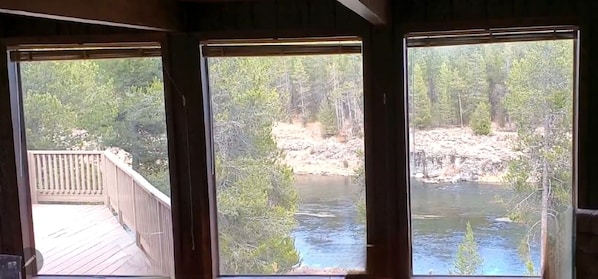 A room with three large windows overlooking a natural landscape with a river and forest.