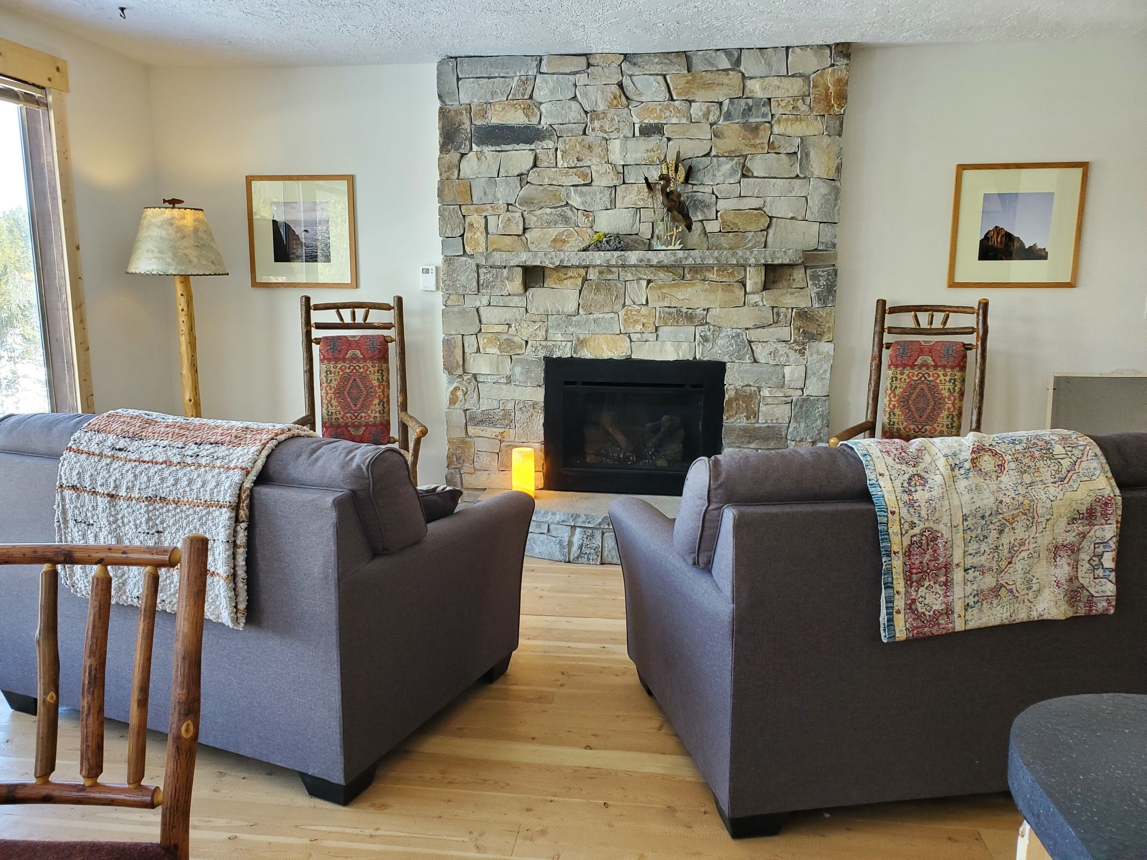 A living room with two grey sofas, a stone fireplace, and a wooden floor.