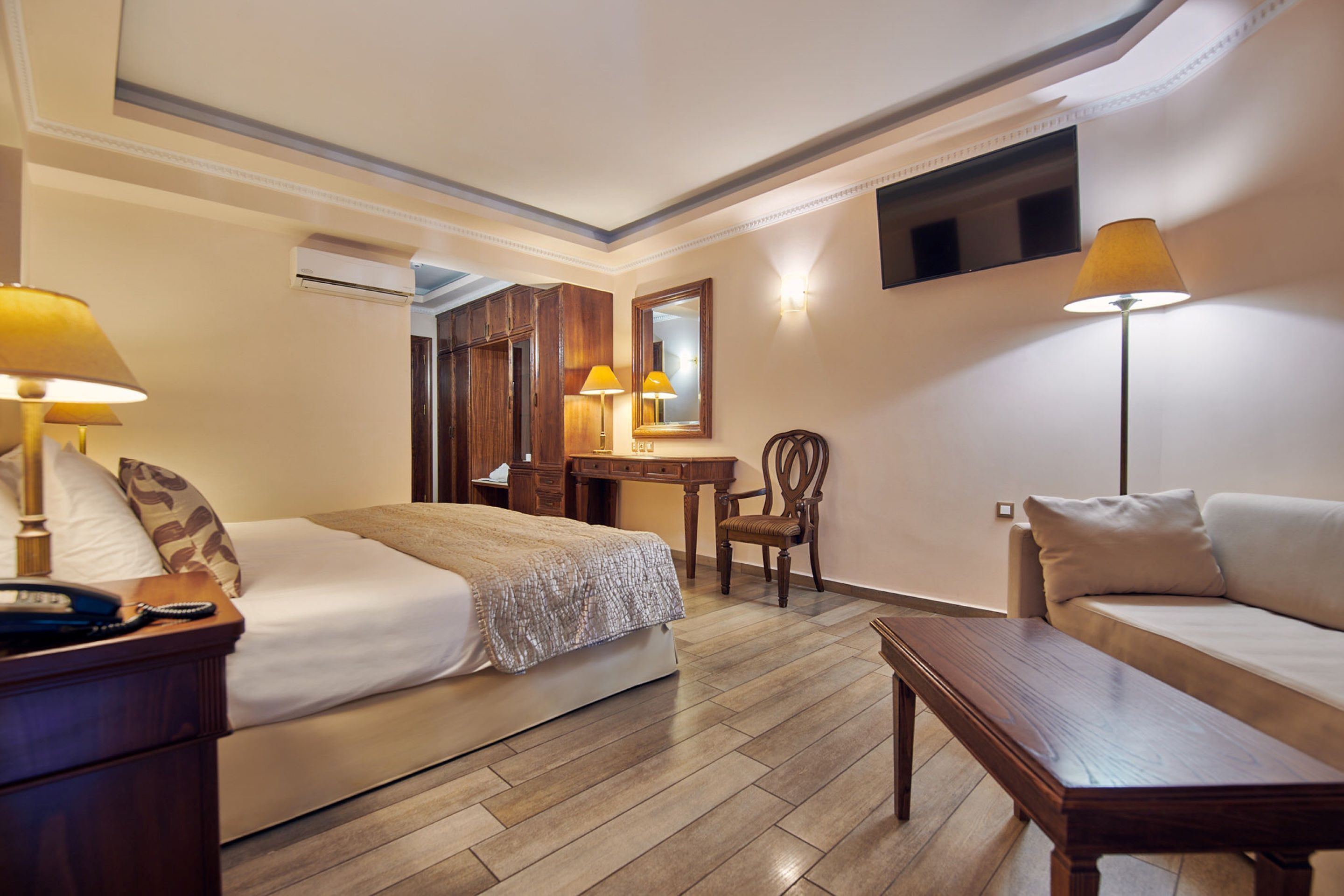 A hotel room with a bed, a desk, a chair, a sofa, and a nightstand.