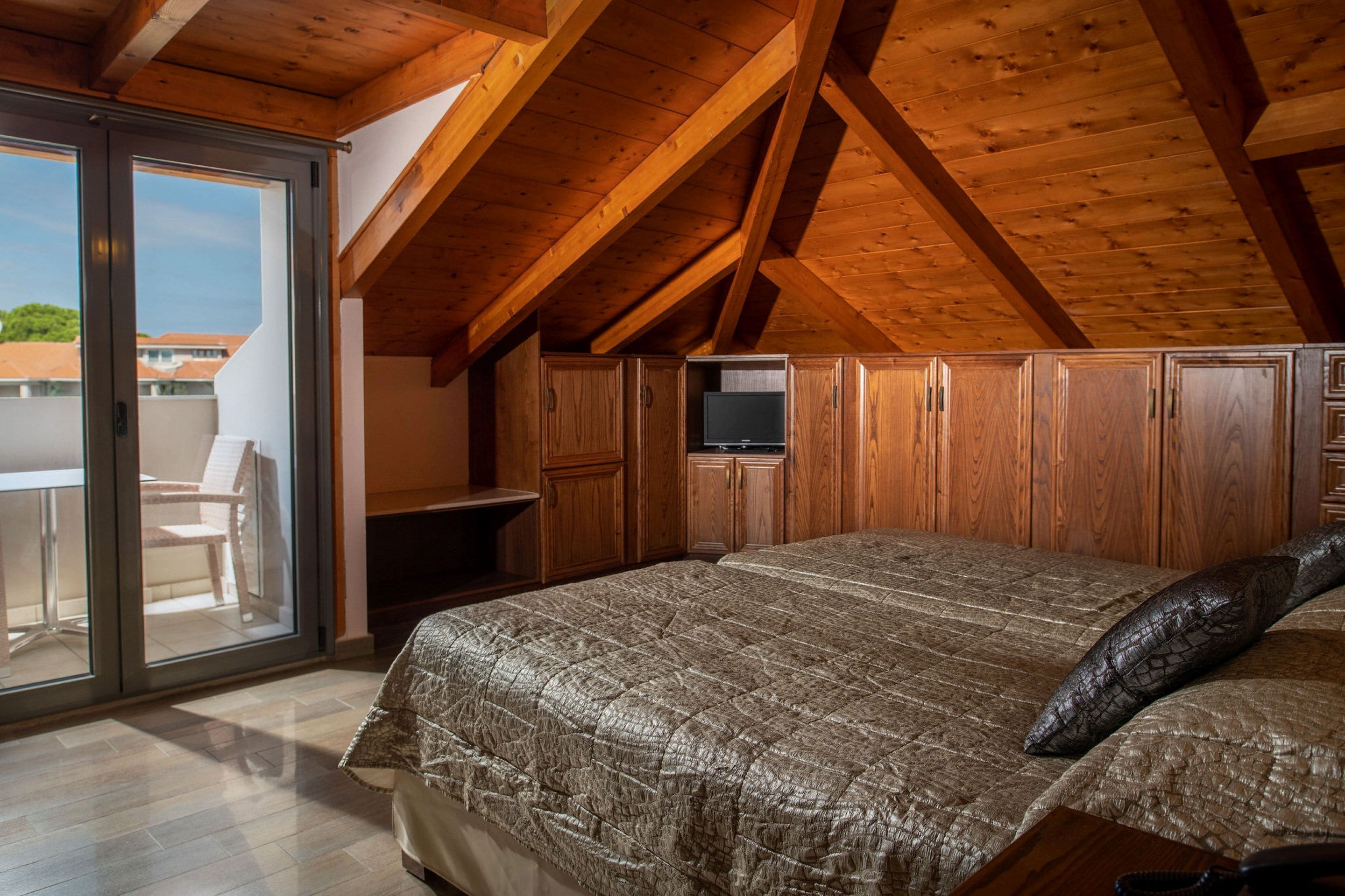A bedroom with a large bed, wooden ceiling beams, and a sliding glass door leading to an outdoor area.