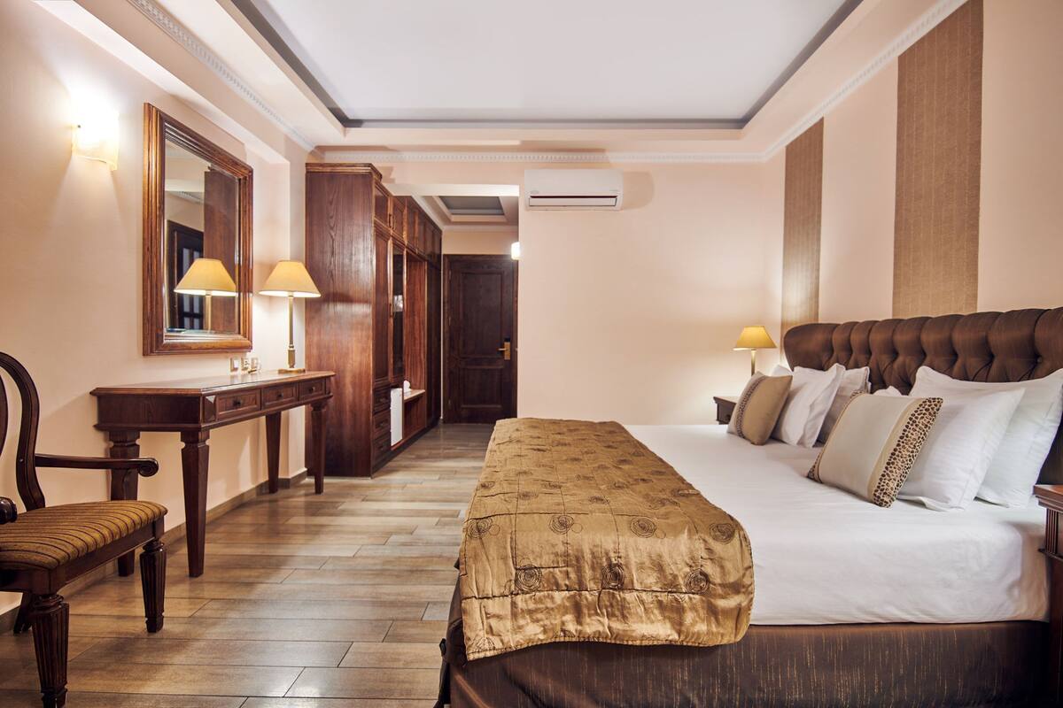 A hotel room with a large bed, a desk with a lamp, a chair, and a mirror.
