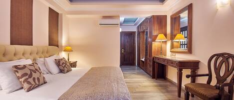 A hotel room with a large bed, a wooden chair, a desk with a lamp, and a mirror.