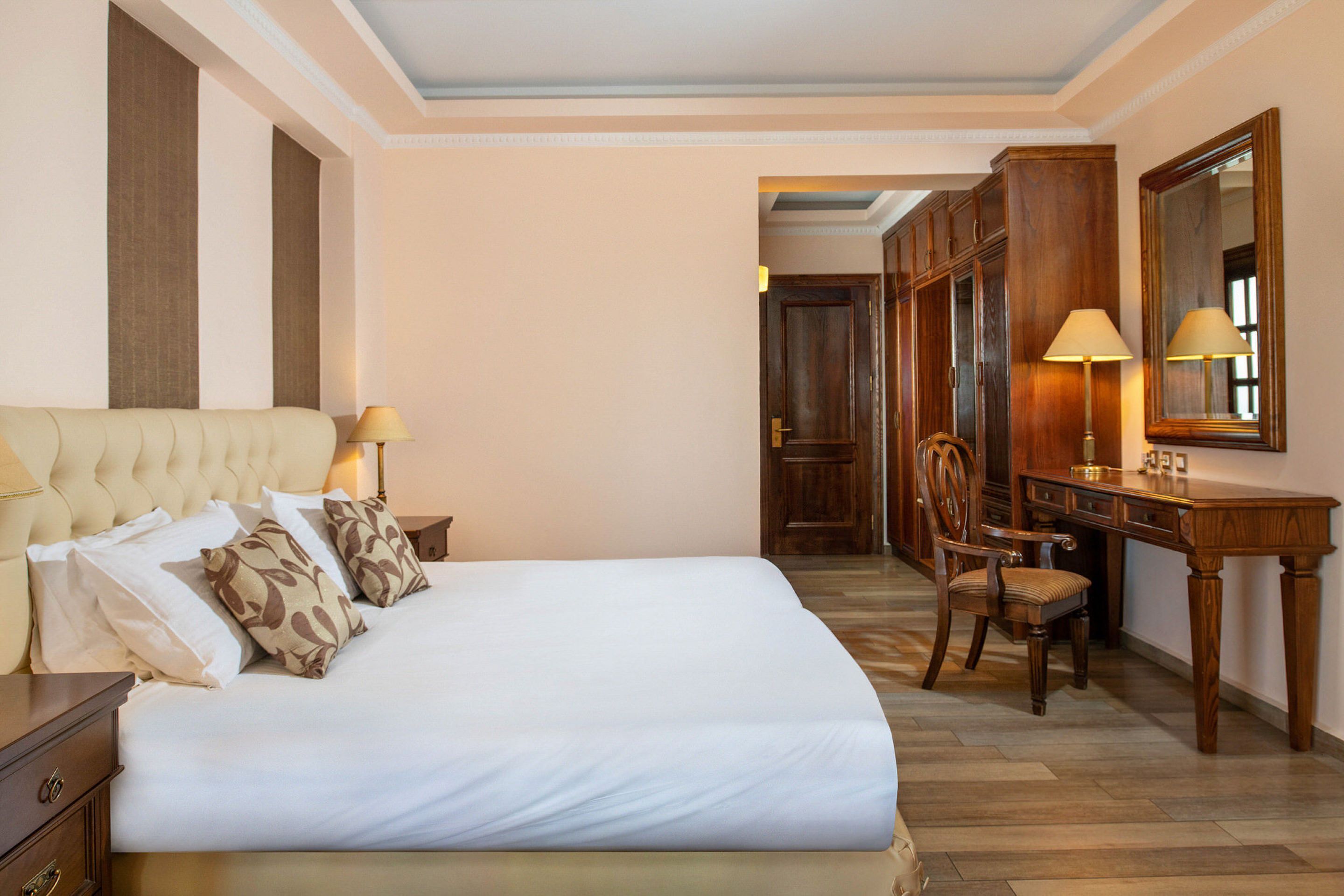 A hotel room with a large bed, a desk, a chair, and a wardrobe.