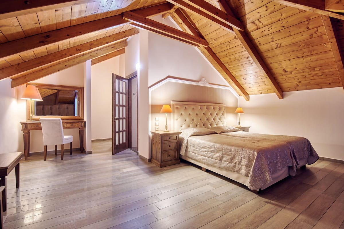 A bedroom with a wooden ceiling, a bed, a nightstand, a chair, and a desk.