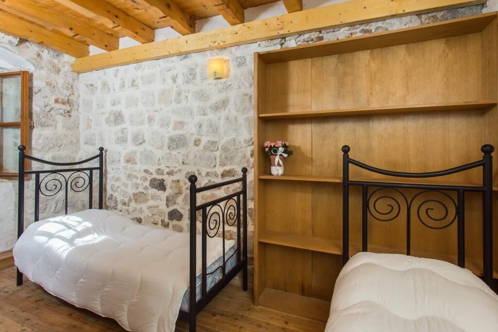 Una habitación rústica con dos camas, paredes de piedra, vigas de madera y una estantería con un jarrón.