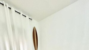 A room with a beige sofa, white curtains, a radiator, and a wooden floor.