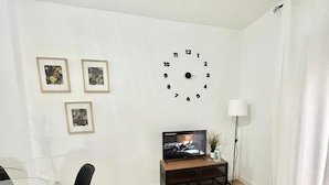 A living room with a wooden floor, a black chair, a TV on a wooden stand, and three framed pictures on the wall.