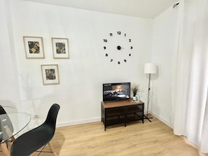 A living room with a wooden floor, a black chair, a TV on a wooden stand, and three framed pictures on the wall.