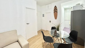 A room with a sofa, a glass table with chairs, a door, and a wall-mounted decorative item.